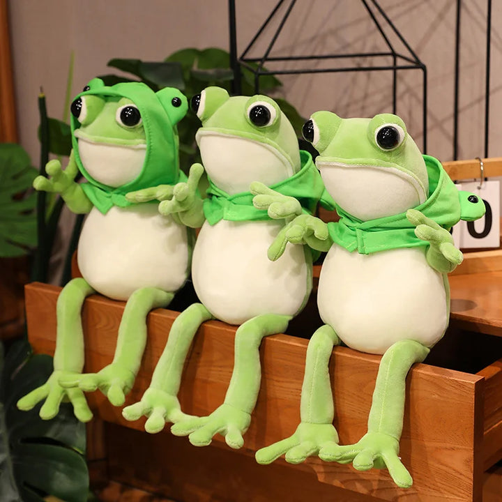 Une adorable peluche grenouille verte aux grands yeux noirs et à la cape verte, posant avec ses pattes avant tendues