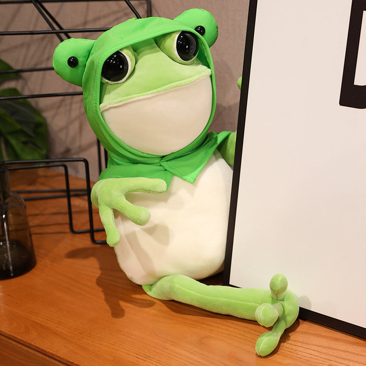 Une adorable peluche grenouille verte aux grands yeux noirs et à la cape verte, posant avec ses pattes avant tendues