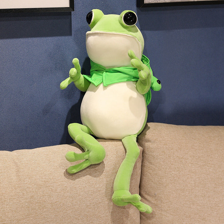 Une adorable peluche grenouille verte aux grands yeux noirs et à la cape verte, posant avec ses pattes avant tendues