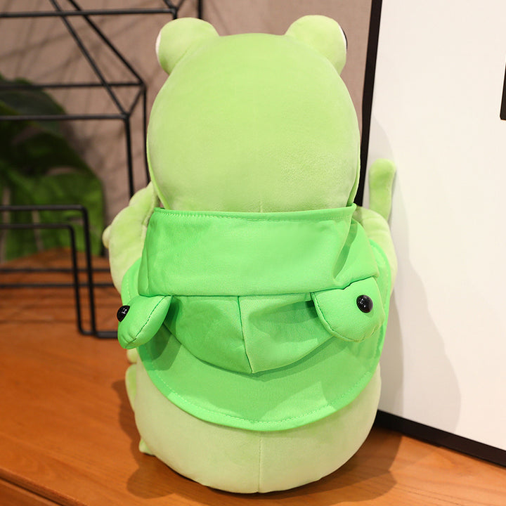 Une adorable peluche grenouille verte aux grands yeux noirs et à la cape verte, posant avec ses pattes avant tendues