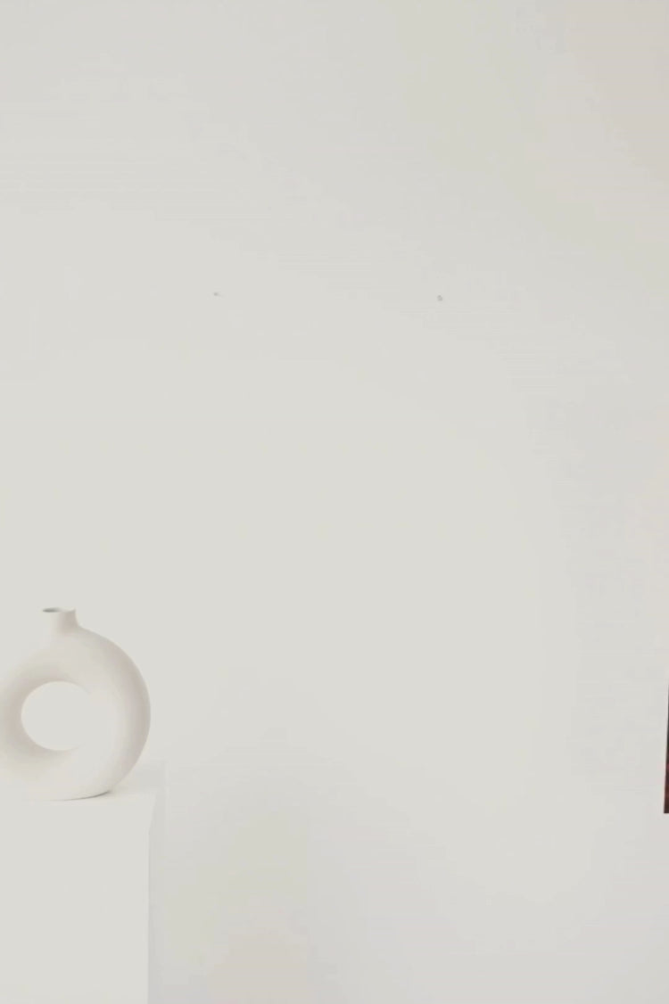 Un chemin bordé de feuilles rouges et dorées serpente vers une cabane pittoresque, tandis qu'une rivière scintillante traverse des prairies paisibles où les vaches se prélassent sous un ciel d'automne éclatant